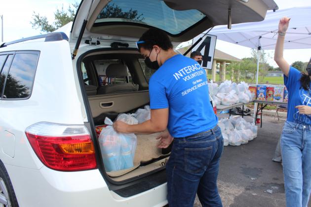 A volunteer from New Dimensions High School places a bag of food into a car truck at Friday's FarmShare food giveaway at Archie Gordon Park in Buenaventura Lakes. PHOTO/KEN JACKSON