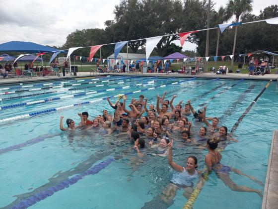Coach Lee Stephenson (center trophy) took a dunk with his swimmers to celebrate Harmony’s team championships. PHOTO/J. DANIEL PEARSON