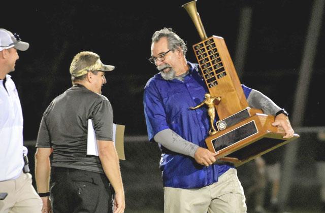 Don Simon carries the Brass Bugle Trophy to his team to celebrate the 44-0 win over St. Cloud in the 2022 regular-season finale, the last of Simon’s 33 coaching wins with the Longhorns. PHOTO/KATIE WHITT WILLIAMS