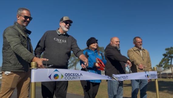 Commissioner Viviana Janer (center) joined Arnco Construction representatives Tuesday to officially cut the ribbon and lead a walk along the new walking trail in 65th Infantry Veterans Park Tuesday. (Photo/Osceola County) 
