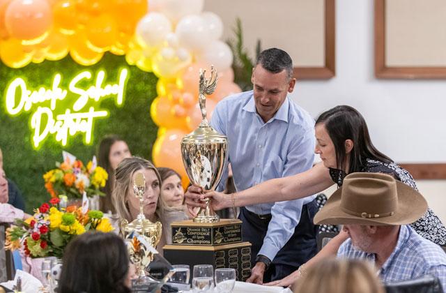 Harmony Principal Laurel Ramsey and Athletic Director Joey James work to find a place at their modest-sized table for the less-modest Orange Belt Conference All-Sports Trophy, which the Longhorns won back. (Photo/Taylor McFee)