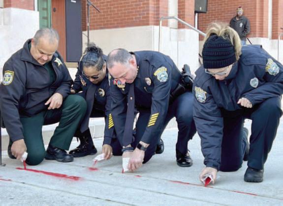 From left, Osceola Sheriff Marco Lopez, Osceola County Corrections Major Yuberky Almonte, St. Cloud Police Chief Doug Goerke and St. Cloud Officer Lin Badman-Paton pour red sand in cracks at the Osceola County Courthouse during Saturday’s Red Sand Project human trafficking awareness event. PHOTO/ST. CLOUD POLICE