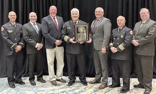 Kissimmee Fire Chief Jim Walls (center with plaque) accepts the Commission on Fire Accreditation International from the Center for Public Safety Excellence assessment team Feb. 27. PHOTO/CITY OF KISSIMMEE