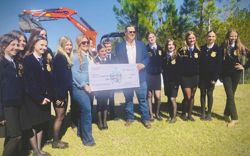 Osceola County Commissioner Ricky Booth, pictured with Harmony Future Farmers of America (FFA) representatives, presents a check for betterment funds Monday to help pay for a new Educational Agricultural Barn at Harmony Middle School, where District Teacher of the Year Kyndall Brown teaches. (Photo/Katie Williams)