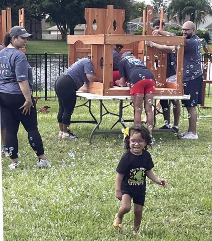 Volunteers from Roc Solid and Amazon built the playset in the Aguilars’ back yard. Once built, Denys Aguilar helps Devyn conquer her new rock-climbing wall. PHOTO/DEBBIE DANIEL