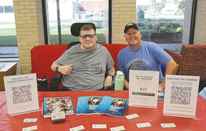 Author Alyx Holliday and his father, Niel Holliday, showed off his cookbook, “See Ya Around the Kitchen: A Cookbook with a Purpose” at the St. Cloud Veteran’s Library. He’s donating $5 from each book sale to FARA research. (Photo/Emely Albelo)