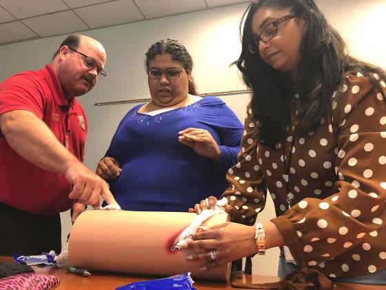News-Gazette Photo/Charlie Reed. From left, Kissimmee Fire Department Lt. Eric Gentry instructs city employees Apneris Salgado and Gita Persaud how to pack an open wound on a training dummy.