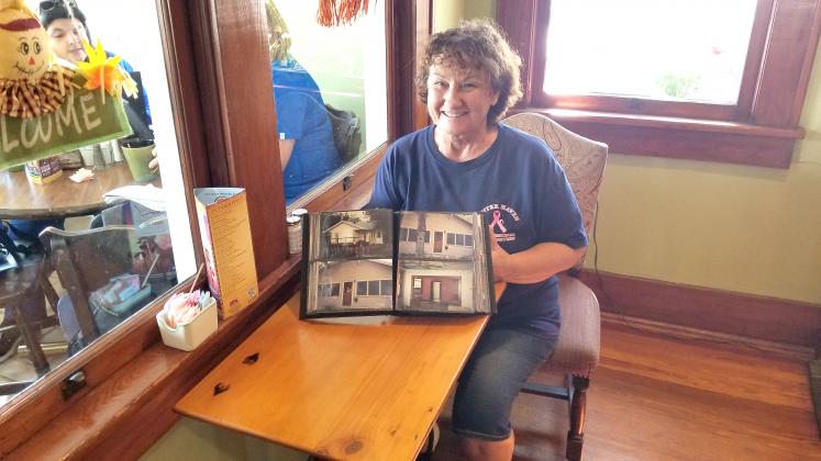 Susan Ramirez, sitting at a table made from original cabinetry of the house that became Susan’s Courtside Café, shows off pictures of the original renovation. PHOTO/KEN JACKSON
