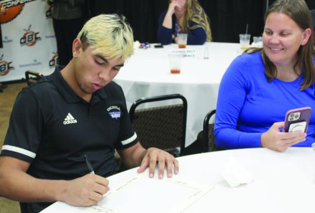 Cooper Haase signs a commemorative picture frame as his mother Shanel Davidson-Haase looks on at the Orange Belt Conference awards ceremony in May. Haase, a four-time state wrestling champion at Osceola High, was also the OBC’s Male Athlete of the Year. PHOTO/KEN JACKSON