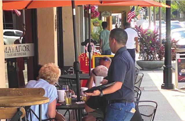 NEWS-GAZETTE PHOTO/BRIAN MCBRIDE A server outside the Matador restaurant in downtown Kissimmee tends to patrons. Due to COVID-19, restaurants can only be at 50 percent capacity as ordered by law.