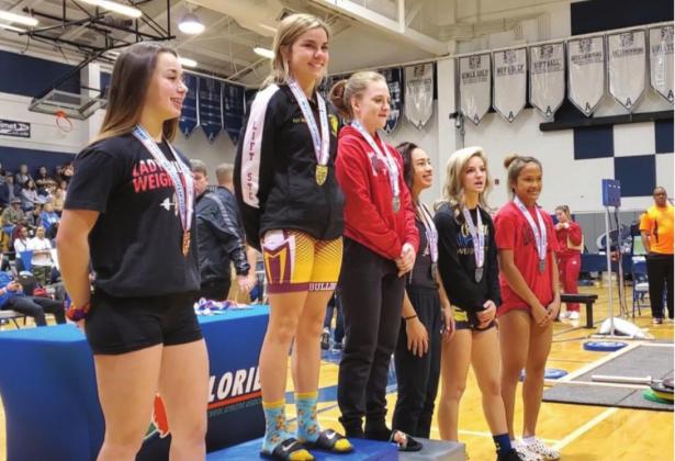 Lady Bulldogs Kaylin White (center) stands atop the podium after winning the 110-pound title at the FHSAA Class 2A Weight Lifting Championship PHOTO COURTESY OF CORY AUN/ST. CLOUD WEIGHTLIFTING