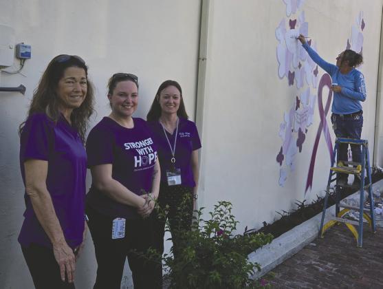 Help Now of Osceola County’s Tammy Douglass, Christina Montolvo and Andie Hinman planted a new bougainvillea tree while artist Jules Ross touches up a domestic violence awareness mural she first painted in 2021 in downtown Kissimmee in honor of Christina’s sister Nicole Montalvo, who was a high-profile violence victim in 2019. (Photos/Ken Jackson)
