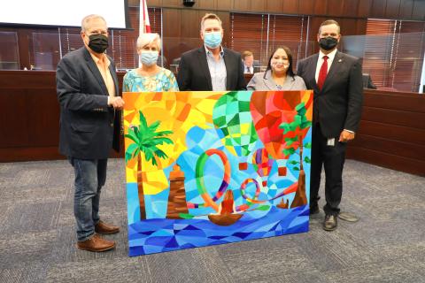 Experience Kissimmee CEO D.T. Minich presents the Osceola County Commission a mural depicting Kissimmee in thanks for its unwavering support during and in the aftermath of the pandemic. PHOTO/EXPERIENCE KISSIMMEE