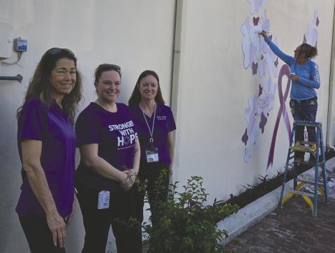 Help Now of Osceola County’s Tammy Douglass, Christina Montolvo and Andie Hinman planted a new bougainvillea tree while artist Jules Ross touches up a domestic violence awareness mural she first painted in 2021 in downtown Kissimmee in honor of Christina’s sister Nicole Montalvo, who was a high-profile violence victim in 2019. (Photos/Ken Jackson)